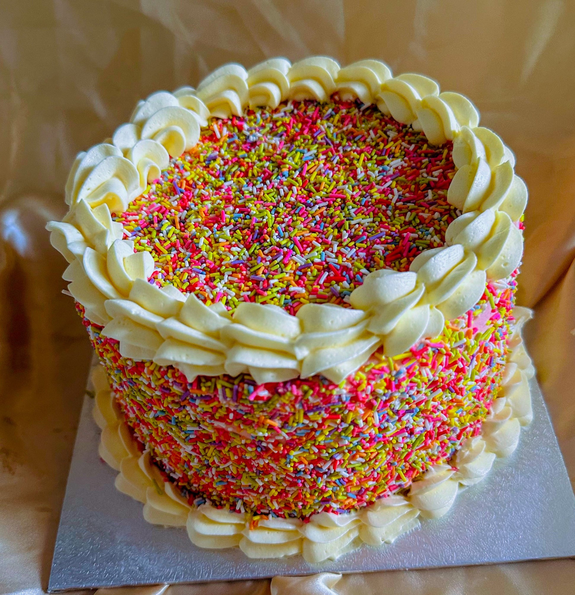 Buy sprinkle birthday cake in Romford and Ilford – colourful sponge covered in rainbow sprinkles with buttercream piping.