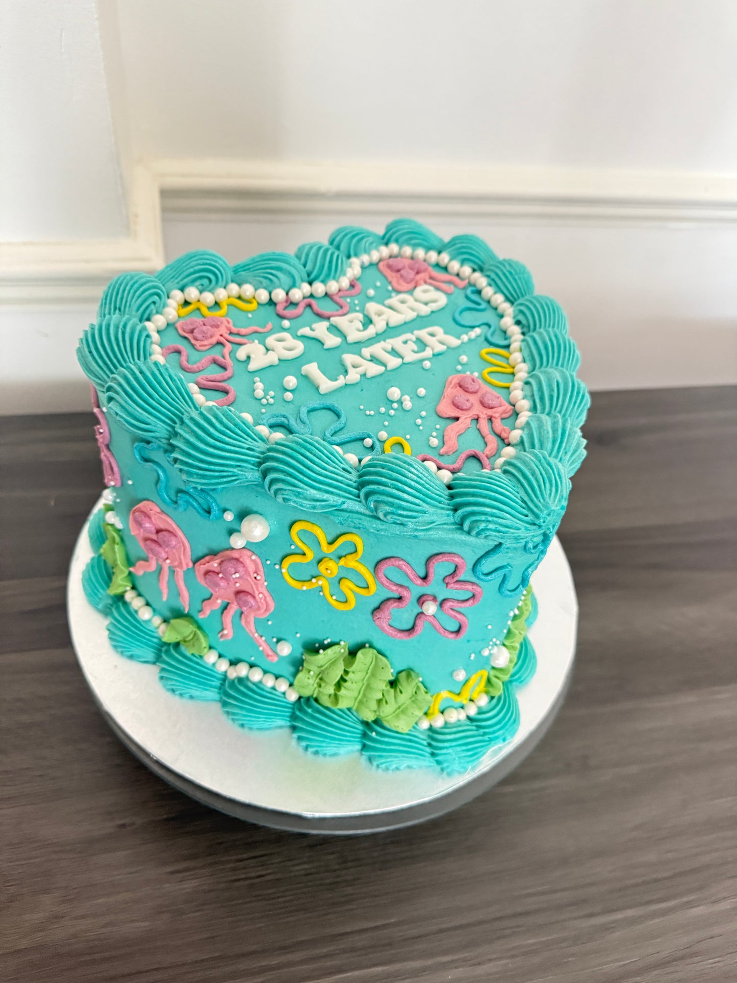 25 Years Later heart-shaped birthday cake with bright blue icing and SpongeBob style decoration – CakeTrays.co.uk same day and next day delivery in Romford, Ilford, and East London.
