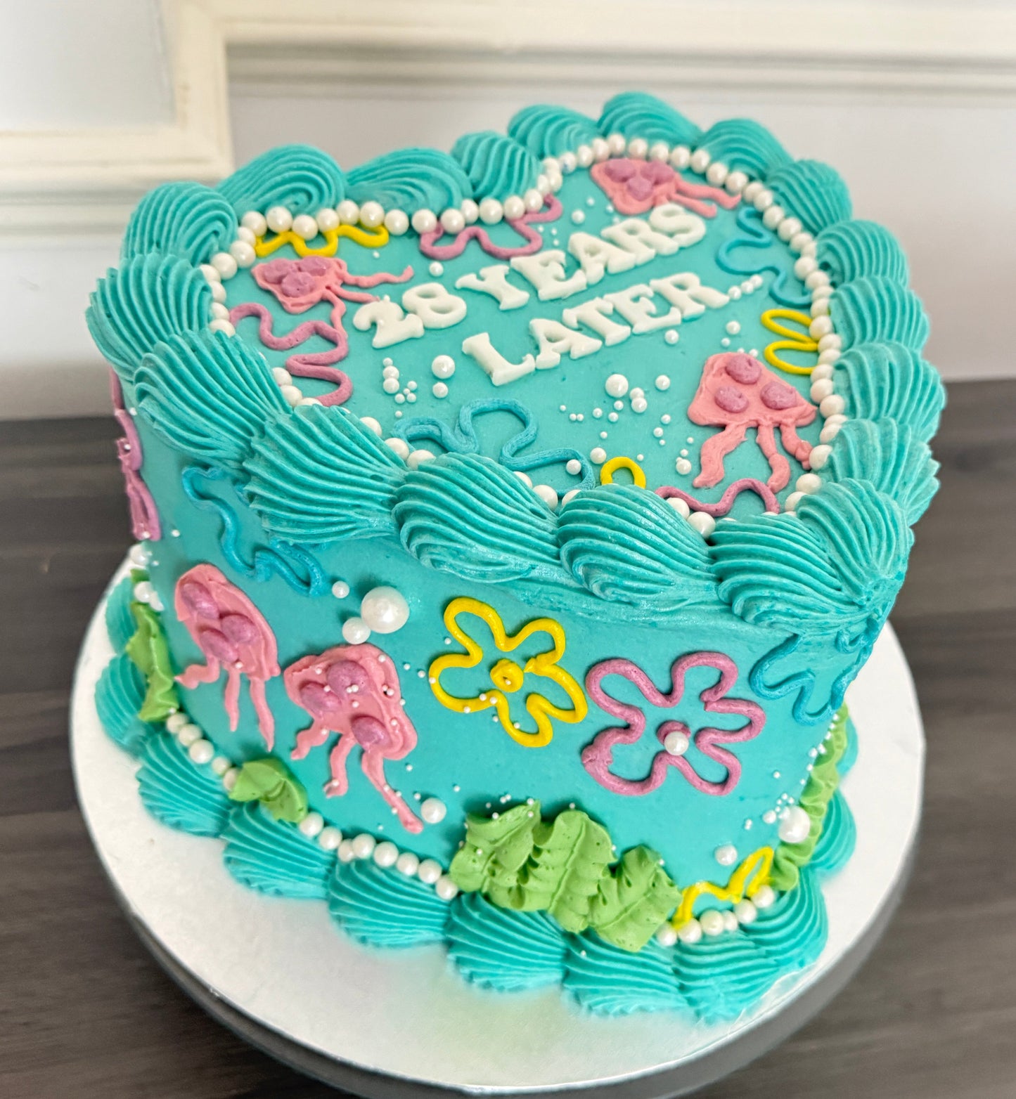 25 Years Later heart-shaped birthday cake with bright blue icing and SpongeBob style decoration – CakeTrays.co.uk same day and next day delivery in Romford, Ilford, and East London.