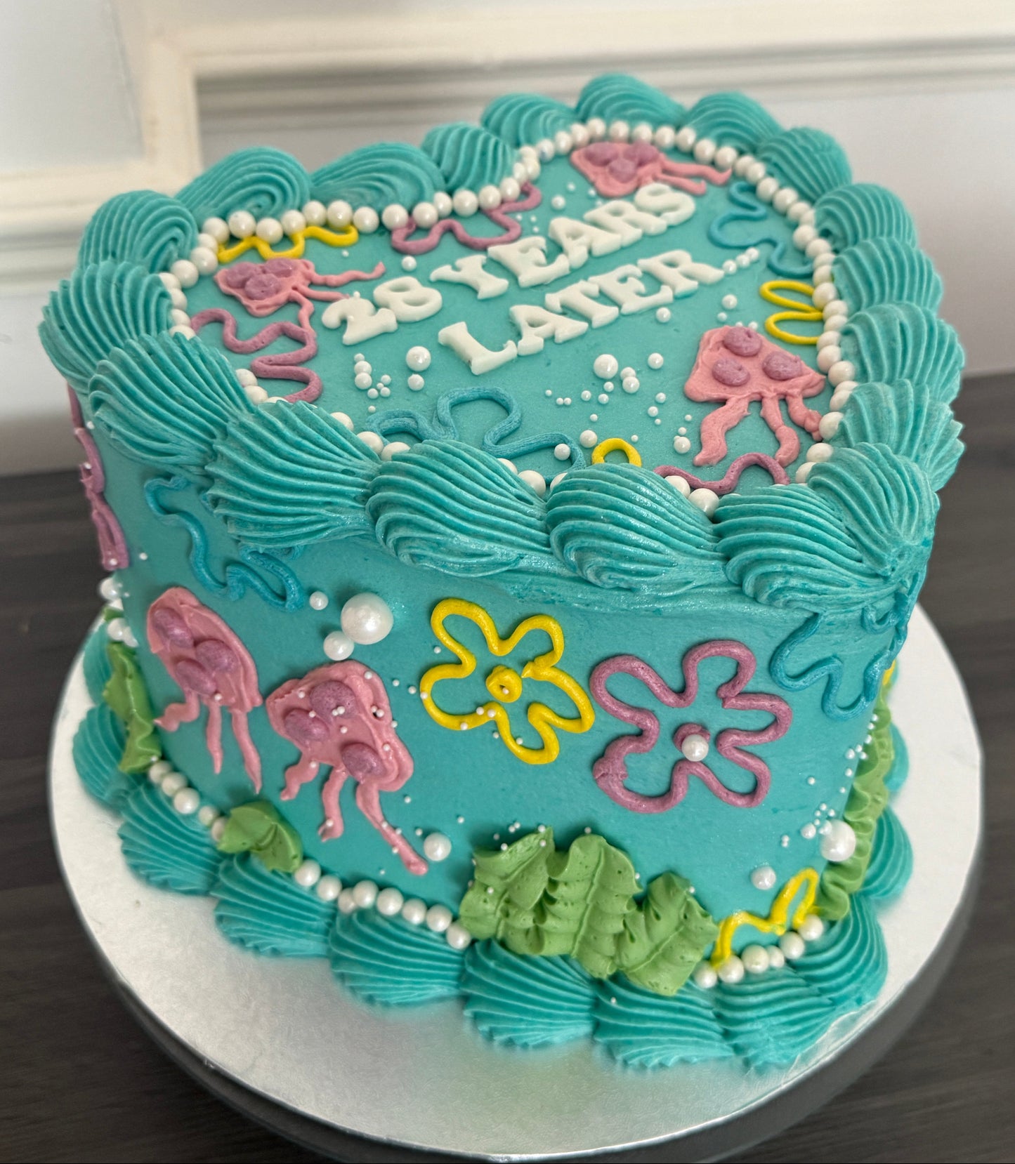 Custom cartoon themed heart cake decorated with colourful flowers, pearls, and ocean-style details – perfect for birthdays with delivery in Barking, East Ham, and East London.
