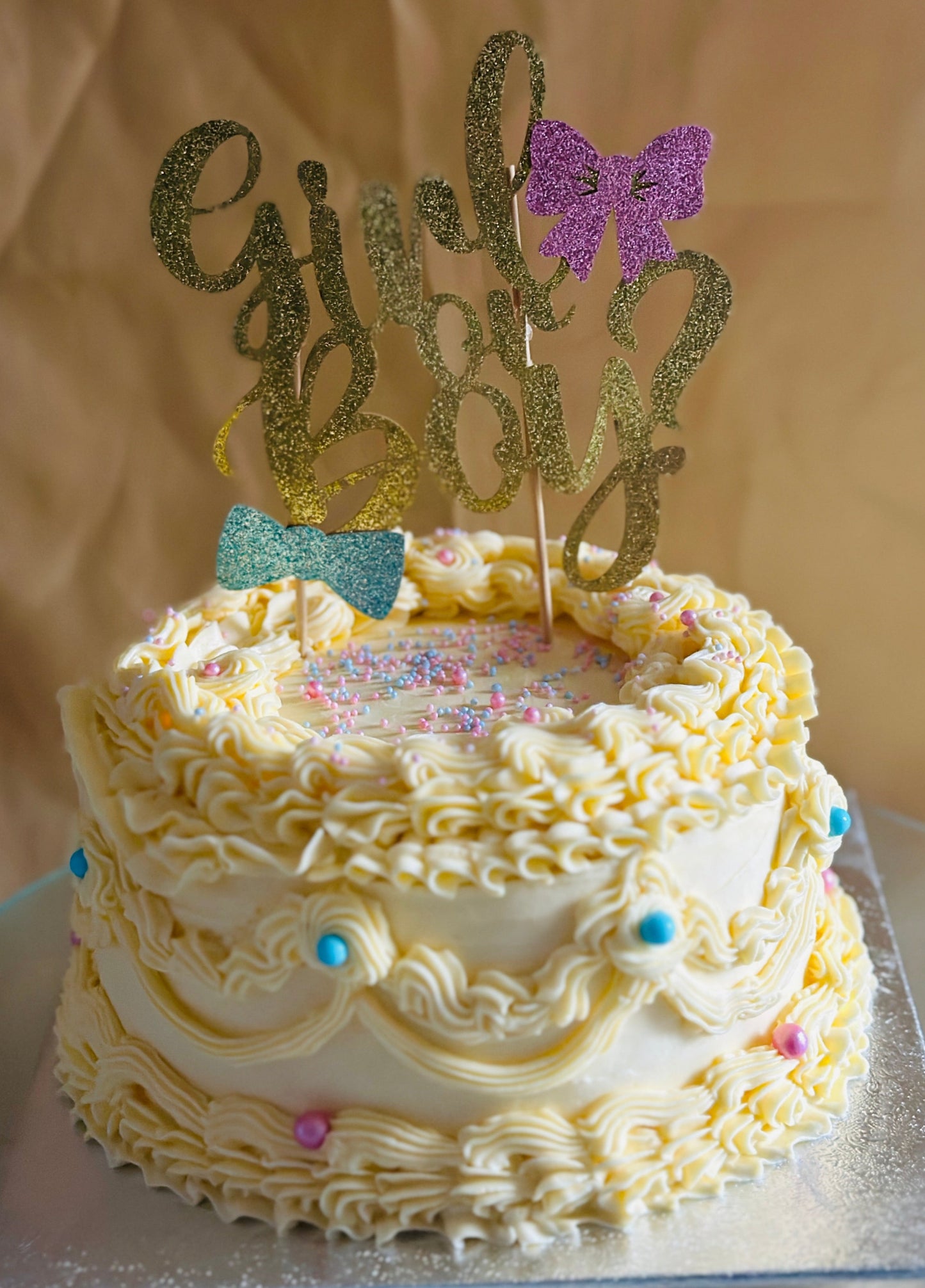 Yellow vintage-style cake for gender reveal with blue and pink pearls