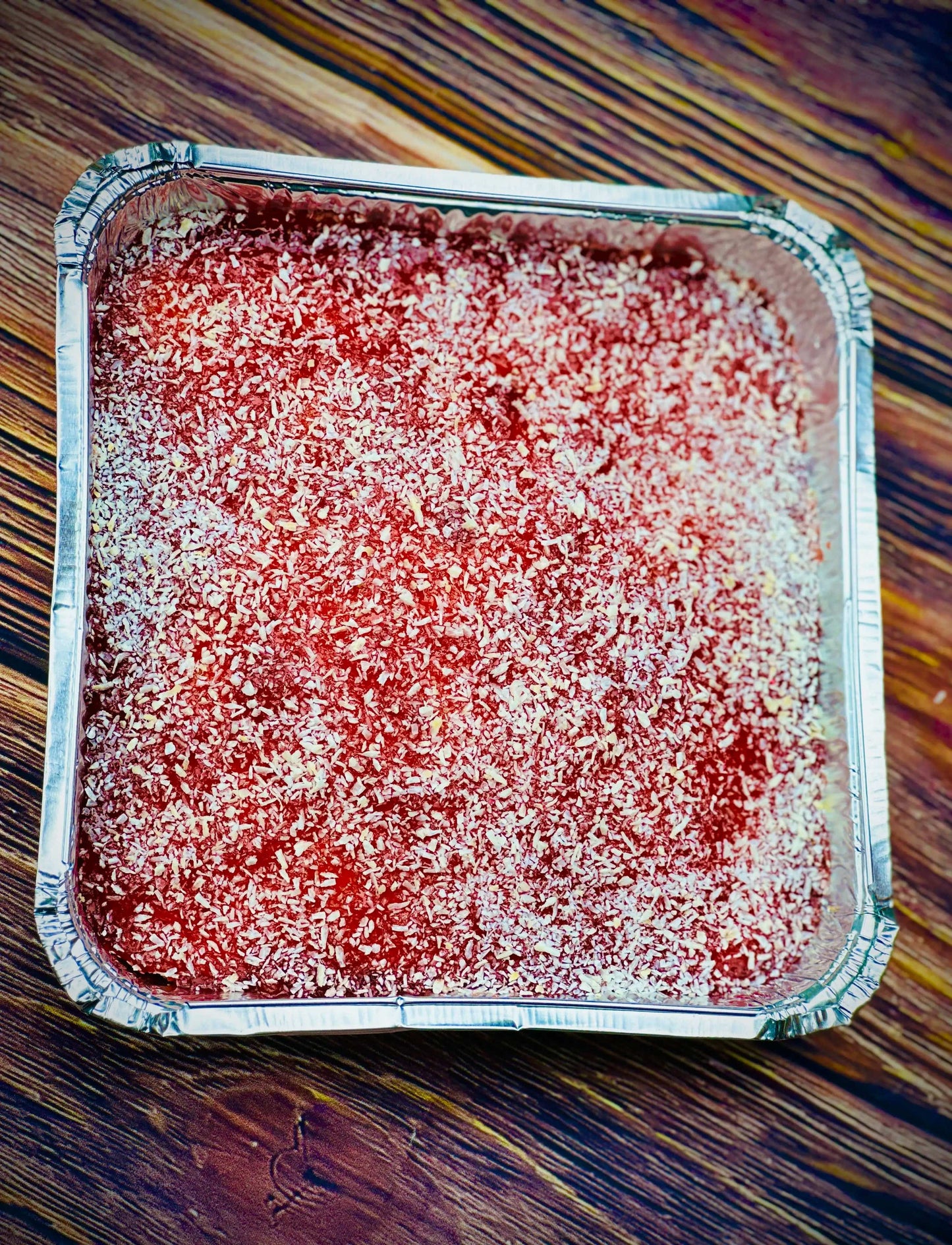 School-style jam and coconut cake topped with coconut on a wooden surface, ready for next day delivery to Walthamstow and Stratford.