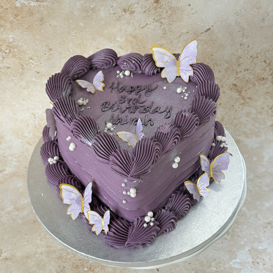 Purple heart shaped birthday cake with piped Happy 3rd Birthday message, lilac butterflies and pearl sprinkles, for a birthday in Plaistow, East London
