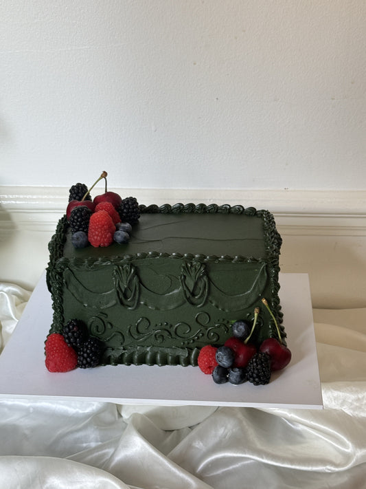 Deep green vintage buttercream birthday cake with hand piped swags and scrollwork, topped with fresh cherries, raspberries, blackberries and blueberries, baked for a birthday in Walthamstow E17
