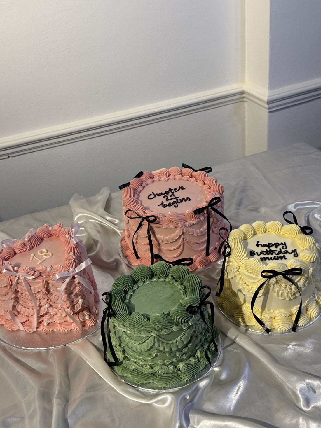 A selection of vintage-style buttercream birthday cakes by Cake Trays delivered in Barking, including a pink 18th, a sage green cake, a Chapter 27 design and a yellow Happy Birthday heart cake with piped ruffles and ribbon bows