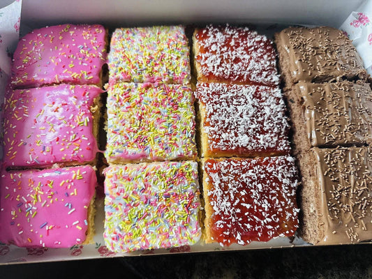 Open box of twelve cake slices in four rows: pink iced, rainbow sprinkle, jam and coconut, and chocolate
