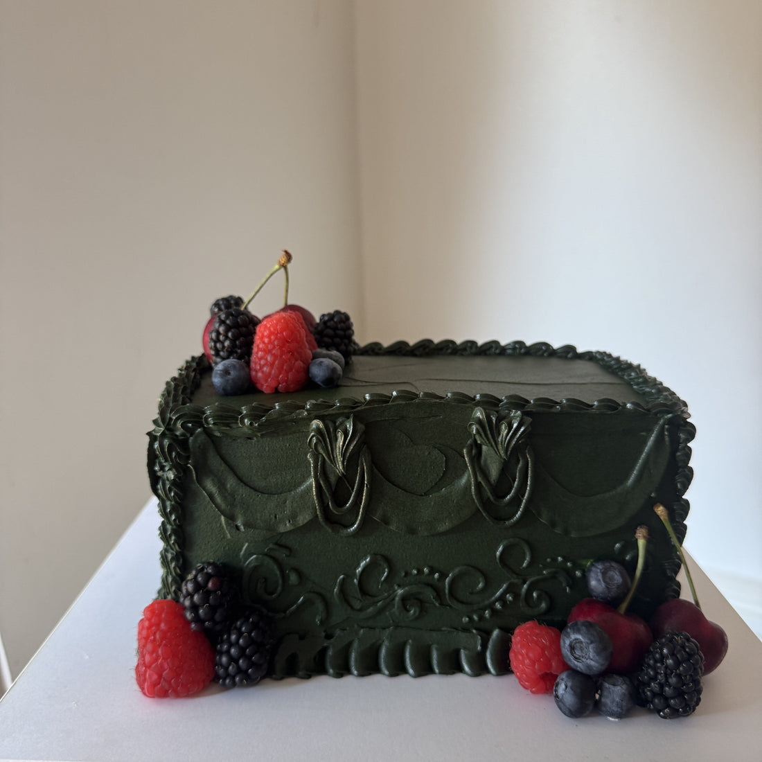 Deep green vintage piped celebration cake with buttercream swags and scrollwork, topped with fresh raspberries, blackberries, blueberries and cherries, baked by Cake Trays for delivery to Manor Park E12 in East London