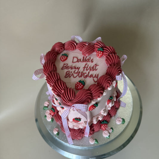 Pink vintage heart first birthday cake with deep red piped shell border, strawberry decorations and gingham bows, piped Dalia's Berry First Birthday, for delivery in Manor Park E12
