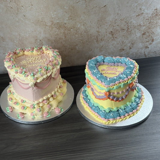 Two vintage heart shaped birthday cakes by Cake Trays, one pink with rosebud piping and one yellow with blue, lilac and green buttercream frills, for a birthday in Goodmayes, IG3
