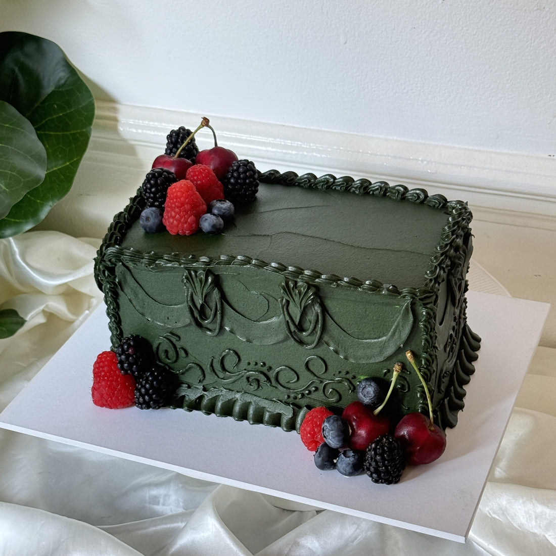 Dark green vintage piped birthday cake topped with fresh raspberries, blackberries, blueberries and cherries, baked by Cake Trays for a milestone birthday in Leyton, East London