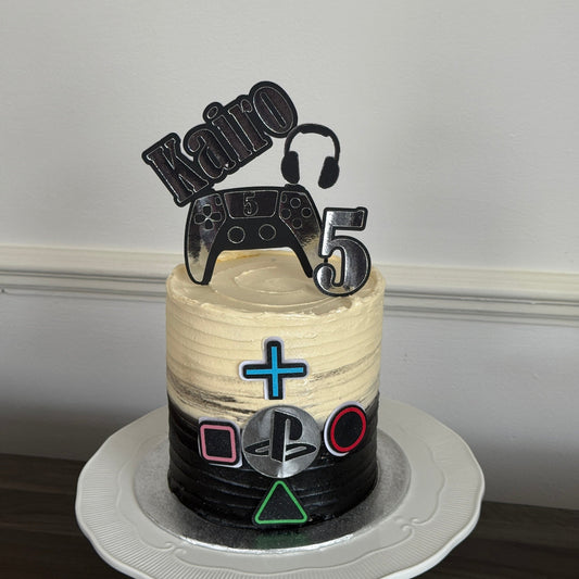 Personalised PlayStation gaming birthday cake in black and cream buttercream with a controller and headset topper and the name Kairo, made by Cake Trays in East London