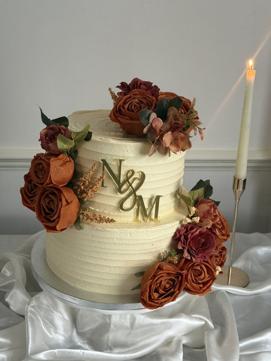 Single tier ivory buttercream Nikkah wedding cake with rust and burgundy roses and a gold N and M monogram, made by Cake Trays in East London