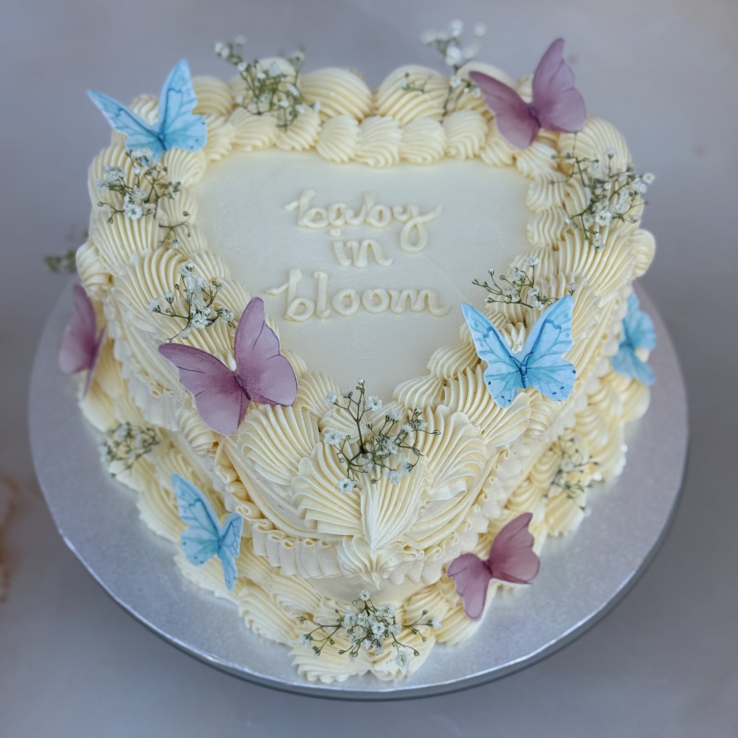 Custom heart-shaped buttercream cake with “Baby in Bloom” piping, ideal for gender reveal celebrations across Romford, Ilford, and surrounding areas.