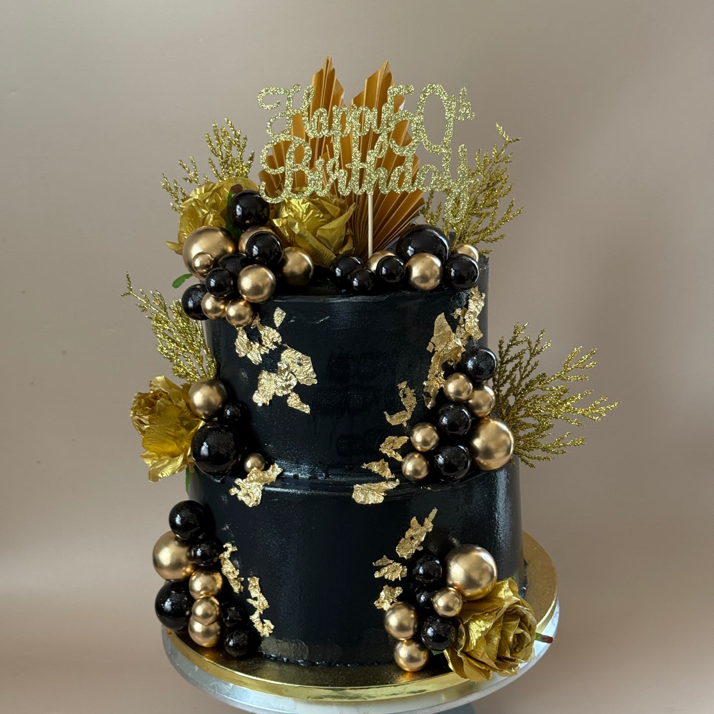 Side view of the black and gold two-tier 50th birthday cake with gold roses and palm fans — custom cakes East London, Romford and Ilford.