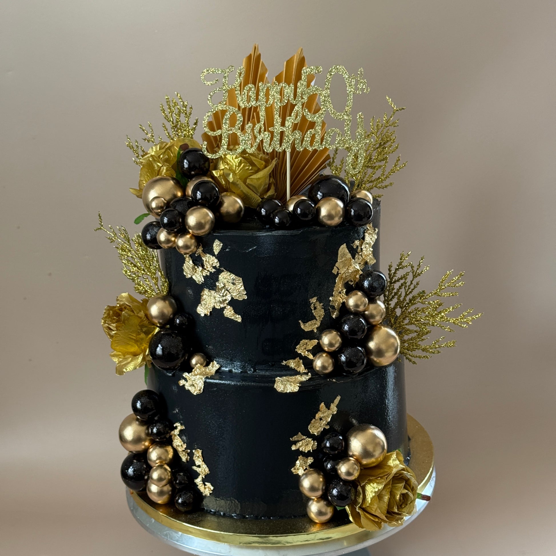 Side view of the black and gold two-tier 50th birthday cake with gold roses and palm fans — custom cakes East London, Romford and Ilford.