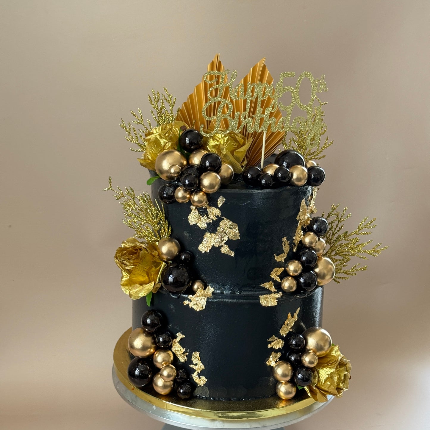 Close detail of gold leaf and black and gold sugar pearls on the two-tier 50th birthday cake — custom cakes East London, Romford and Ilford.