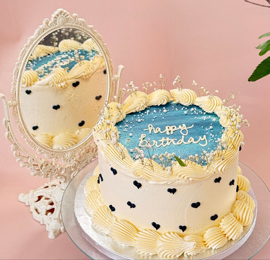 Cream buttercream cake with a blue painted plaque, happy birthday message, piped black hearts and gypsophila — custom cakes East London, Romford and Ilford.