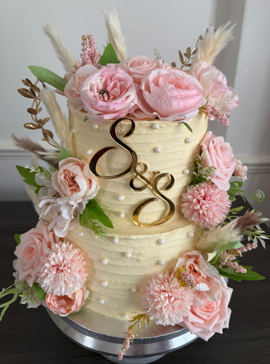 Blush Rose and Pampas two tier ivory buttercream wedding cake with cascading pink florals and personalised S and S gold monogram topper from Cake Trays East London