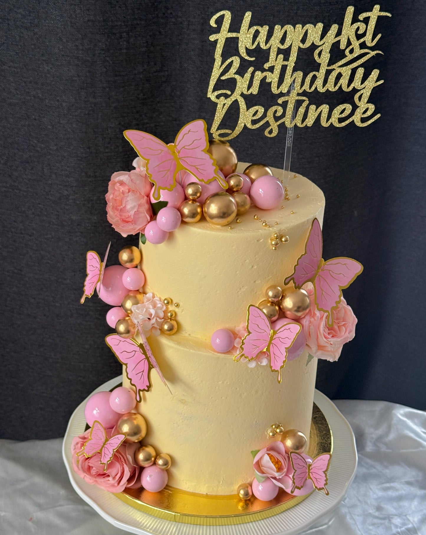 Two tier butter yellow first birthday cake with pink and gold spheres and butterflies, custom cakes East London, Romford and Ilford.