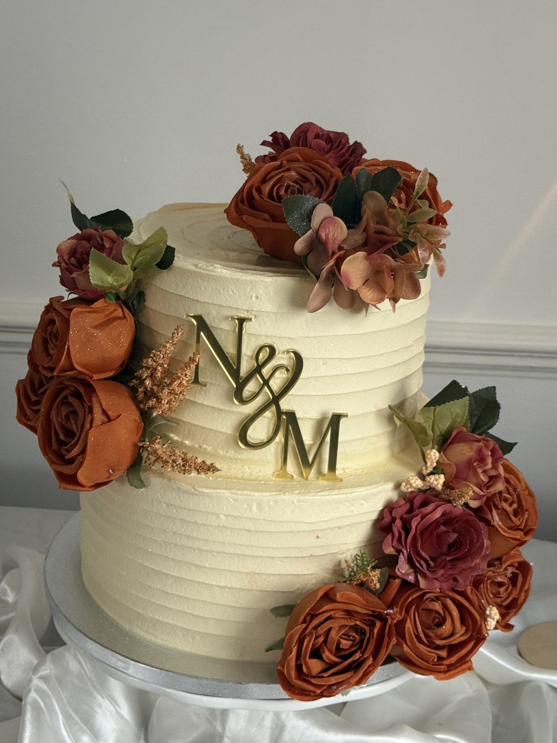 Close-up of the gold initials topper on the Rust Rose Monogram Wedding Cake with ivory buttercream texture and floral accents, personalised wedding cake by Cake Trays.