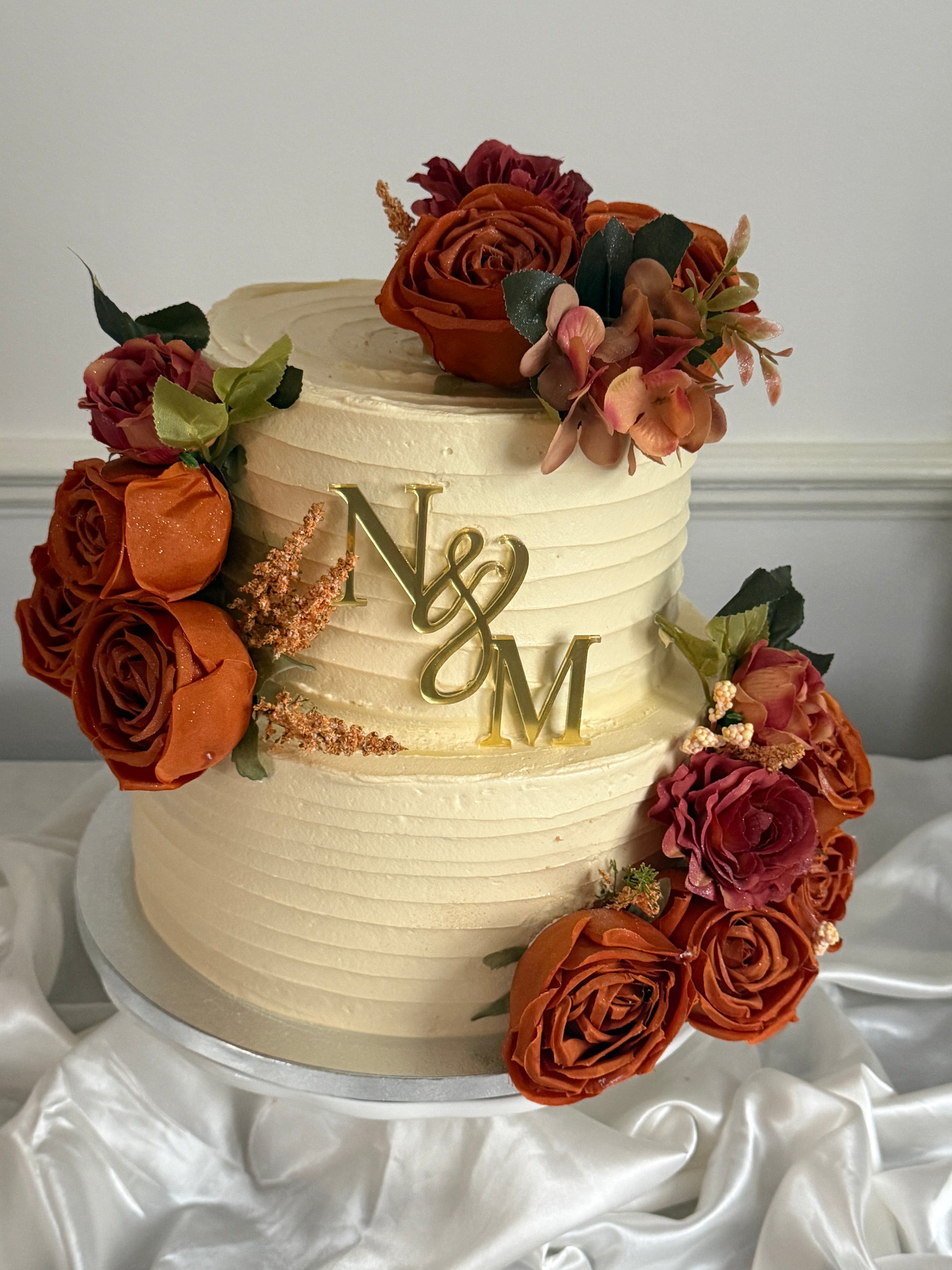 Side view of Rust Rose Monogram Wedding Cake showing rust rose clusters and burgundy flowers on a textured ivory buttercream finish, delivered across Barking and Dagenham.