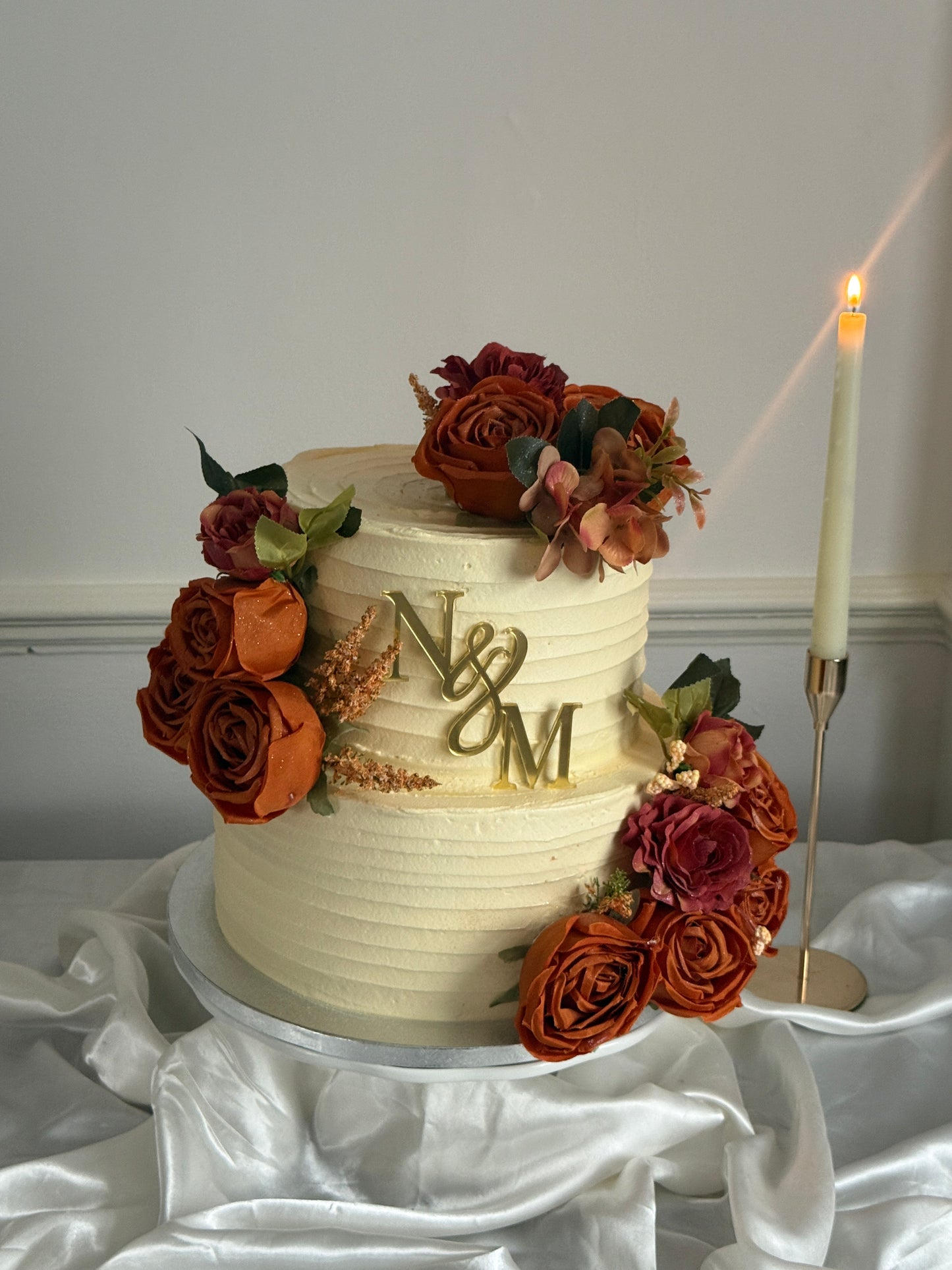 Rust Rose Monogram Wedding Cake styled on a cake stand with candle, gold initials topper and autumn florals, ideal for weddings and nikkahs in East London.