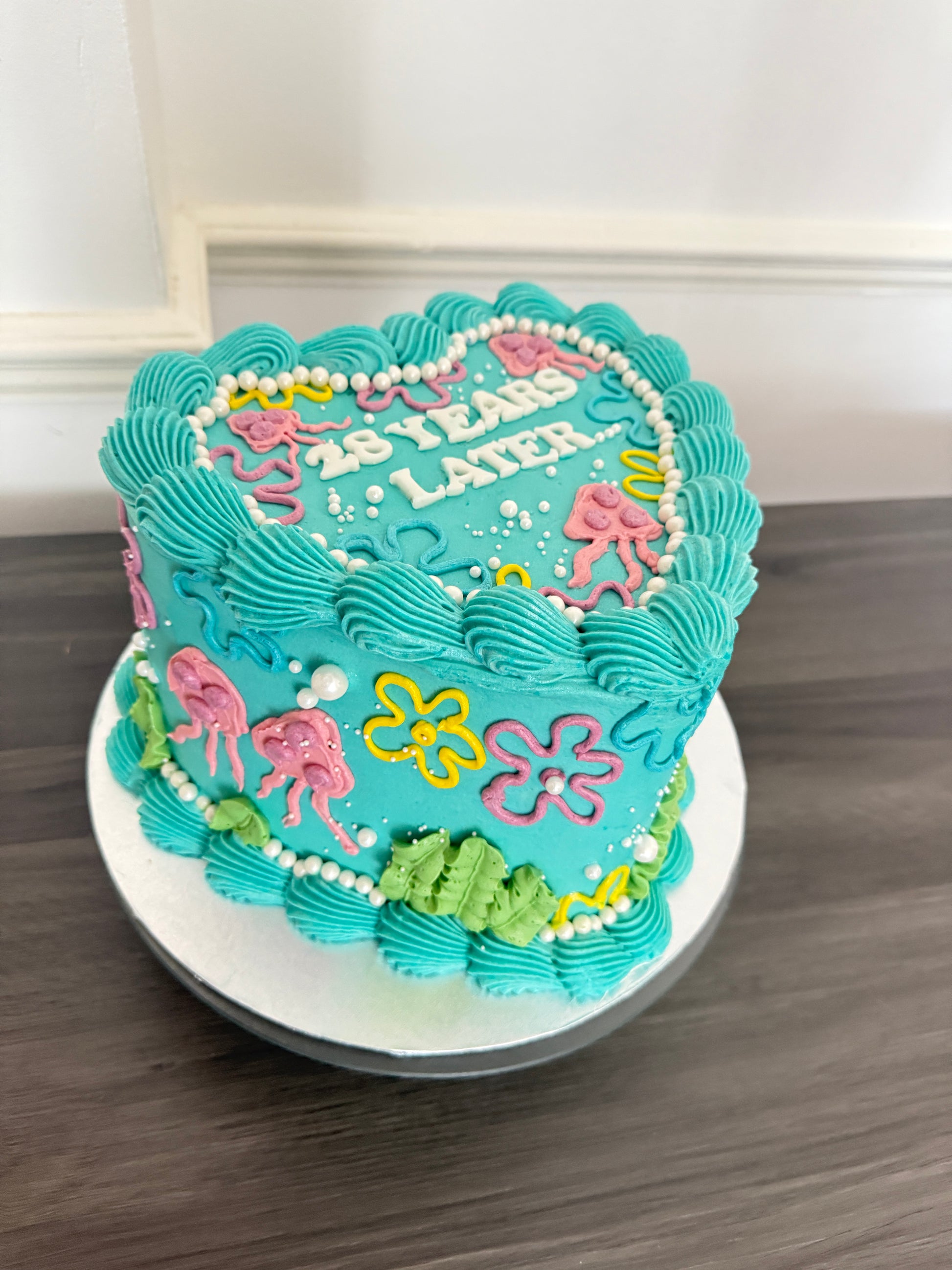 25 Years Later heart-shaped birthday cake with bright blue icing and SpongeBob style decoration – CakeTrays.co.uk same day and next day delivery in Romford, Ilford, and East London.