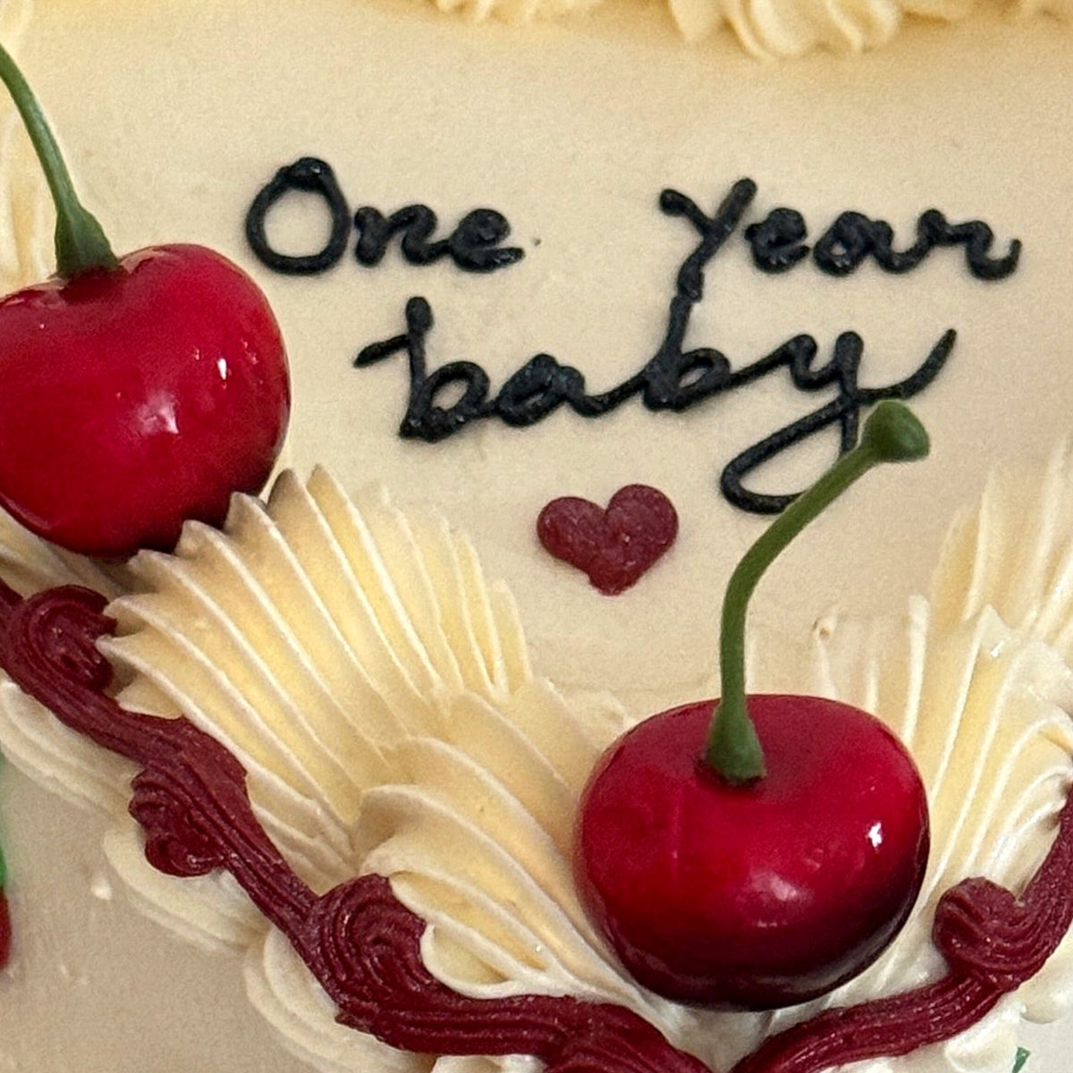 Personalised One Year baby message piped in dark buttercream on a cherry heart cake, delivered to East Ham