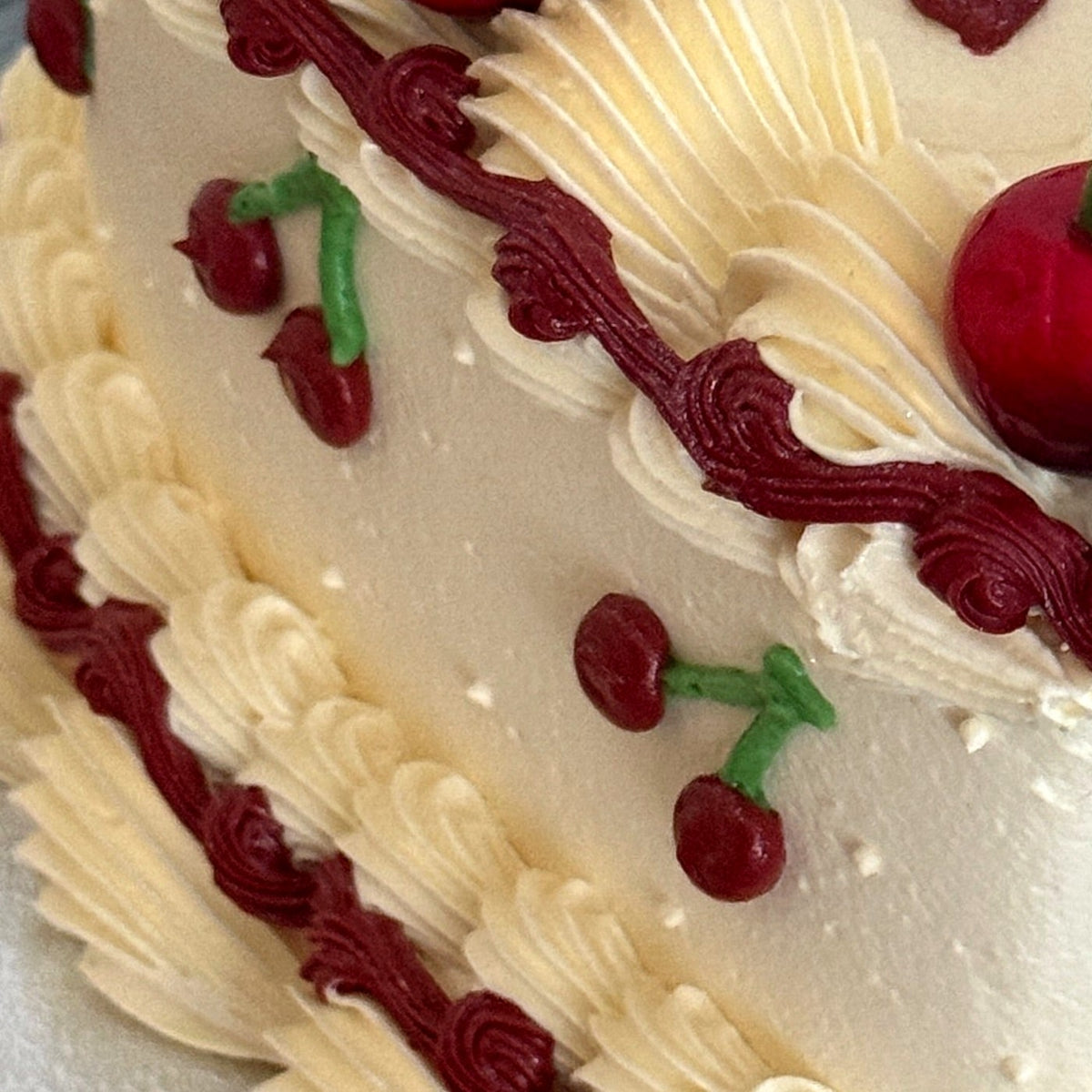 Deep red rope piping and piped mini cherries on a cream vintage heart cake, delivered to Stratford