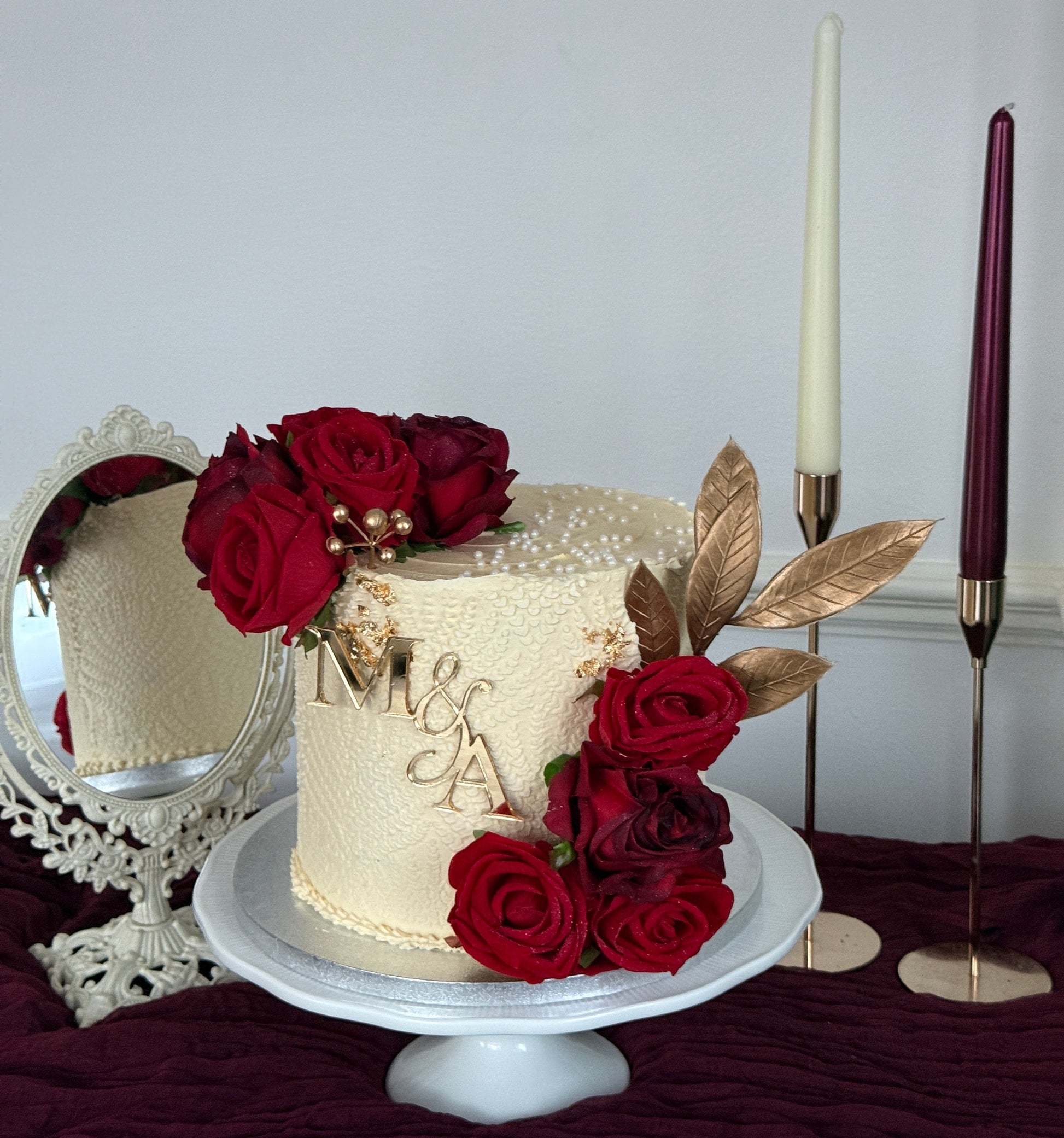 Elegant ivory wedding cake with crimson roses, gold leaf detail and custom monogram topper for Walima and engagement celebrations in East London