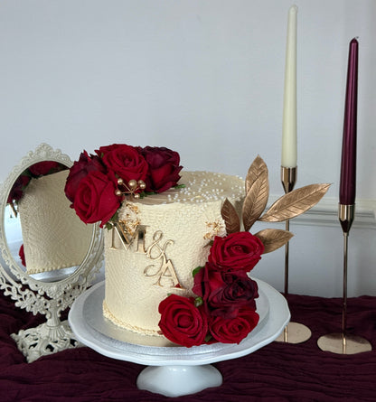 Elegant ivory wedding cake with crimson roses, gold leaf detail and custom monogram topper for Walima and engagement celebrations in East London