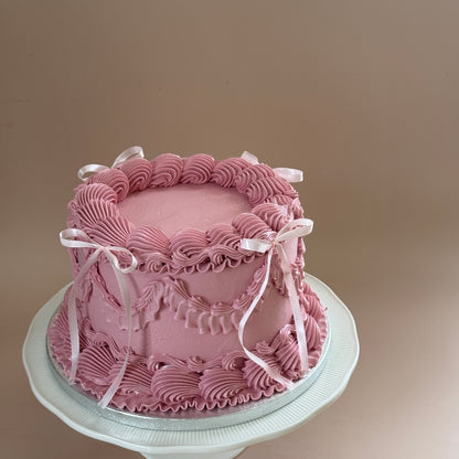 Side view of a dusky pink vintage Lambeth buttercream cake with satin bows on a cake stand — custom cakes East London, Romford and Ilford.