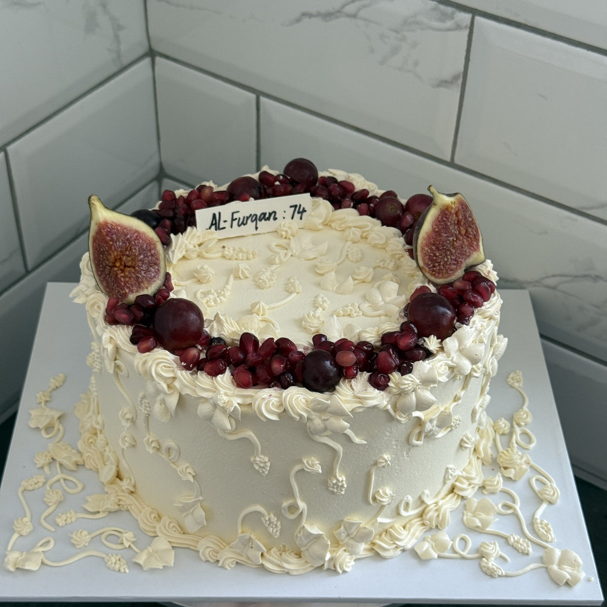 Ivory vintage piped fig and pomegranate cake on a white board, custom cakes East London, Romford and Ilford.