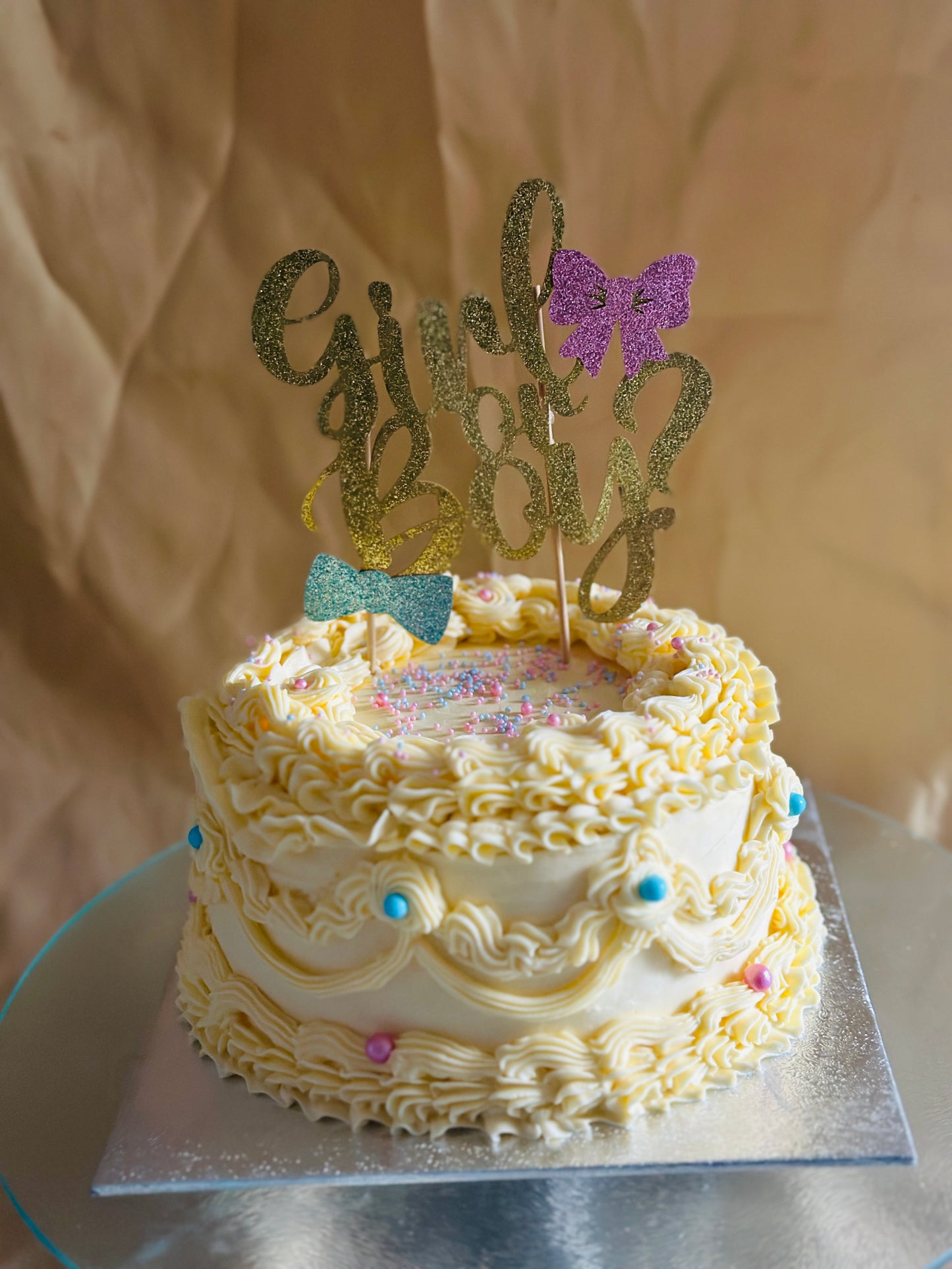 Yellow vintage-style cake for gender reveal with blue and pink pearls