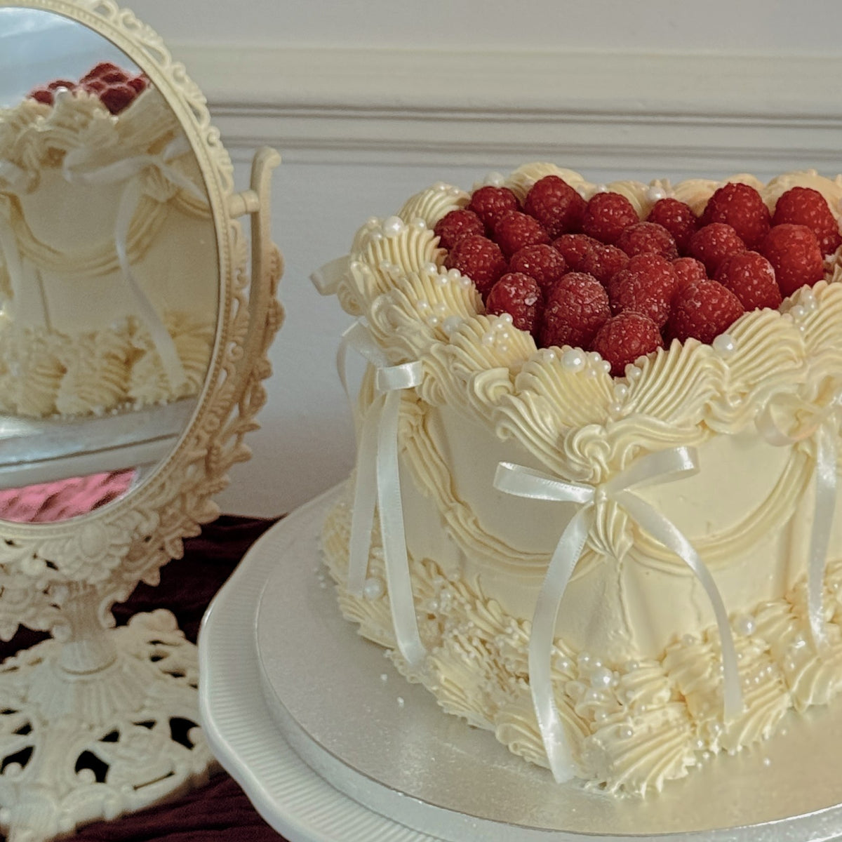 Ivory vintage Lambeth heart cake with fresh raspberries, satin bows and pearls, custom cakes East London, Romford and Ilford.