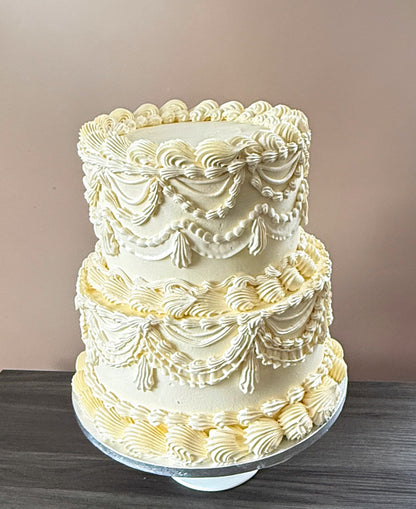 Two-tier ivory buttercream cake piped with vintage Lambeth swags, ruffles and tassels — custom cakes East London, Romford and Ilford.
