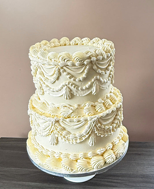 Two-tier ivory buttercream cake piped with vintage Lambeth swags, ruffles and tassels — custom cakes East London, Romford and Ilford.
