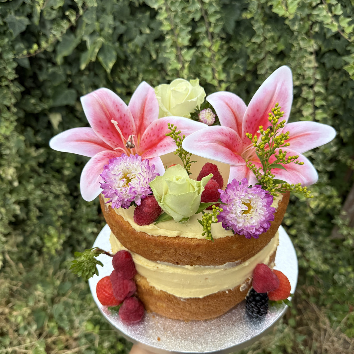 Naked lily and berry cake photographed against a green hedge, custom cakes East London, Romford and Ilford.