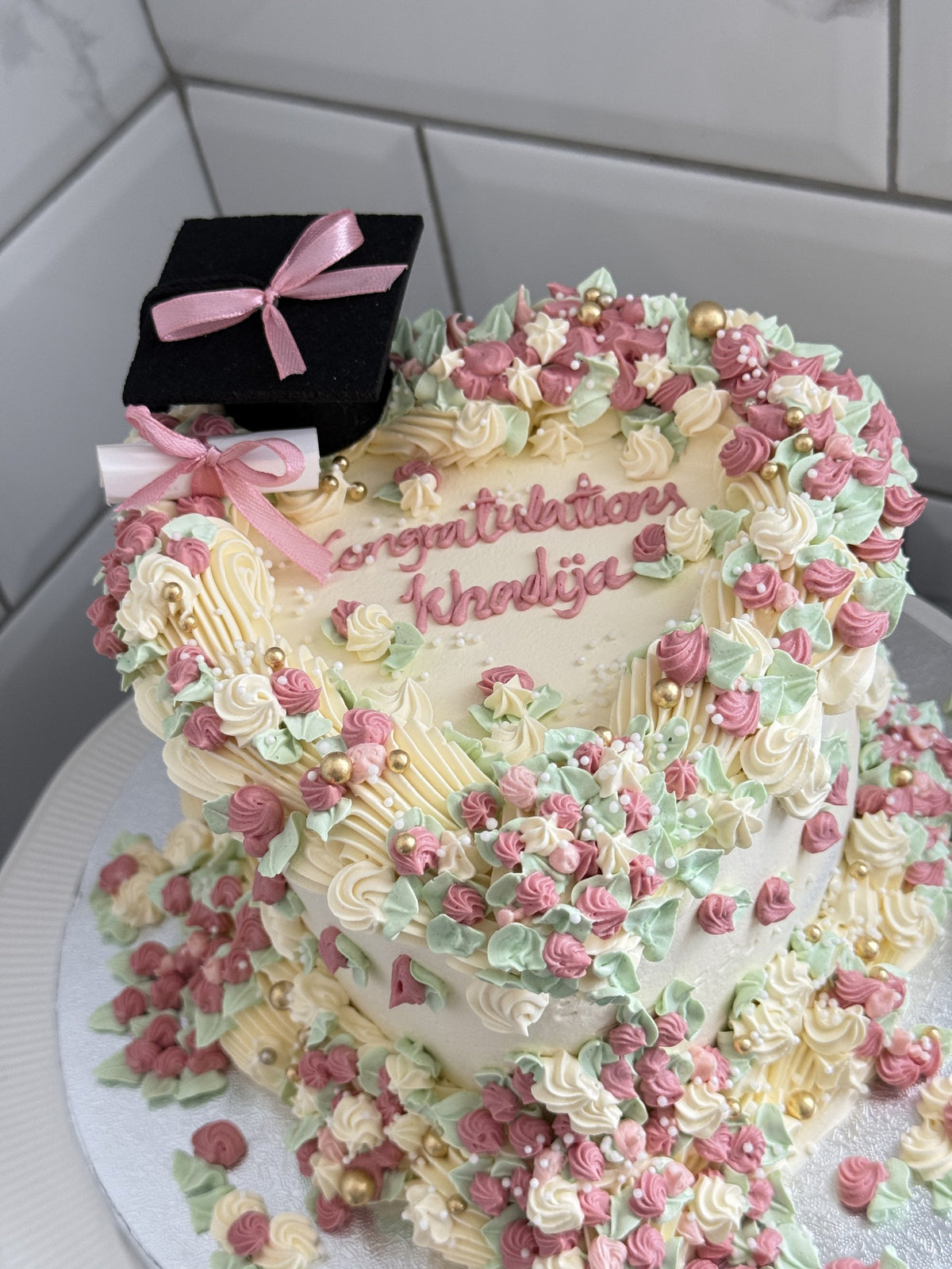 Angled view of the graduation heart cake with pink and sage rosettes, custom cakes East London, Romford and Ilford.