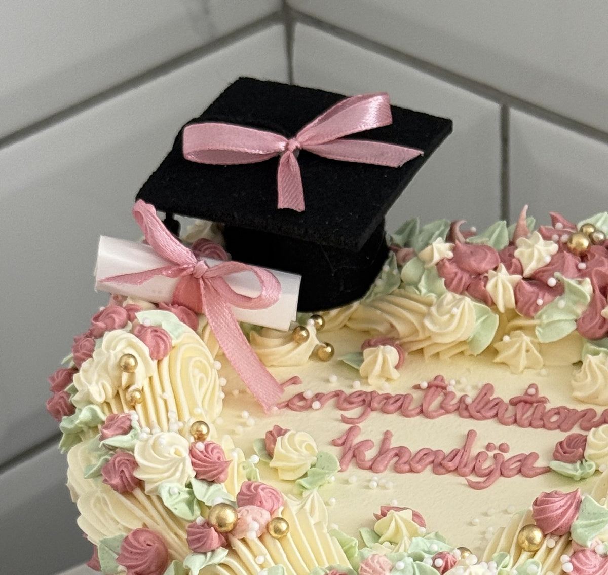 Close up of the mortarboard, pink bow and diploma scroll topper on the heart cake, custom cakes East London, Romford and Ilford.
