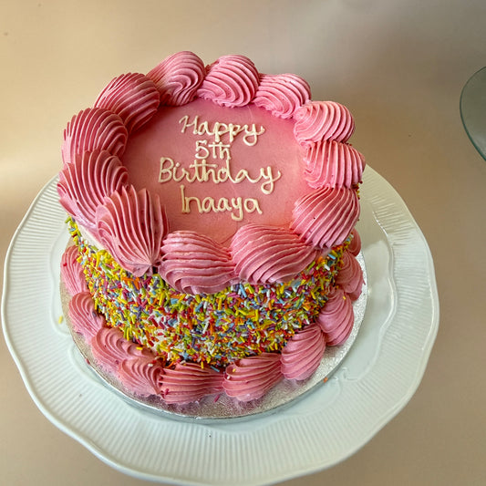 Pink buttercream birthday cake with shell piping and a rainbow sprinkle band — custom cakes East London, Romford and Ilford