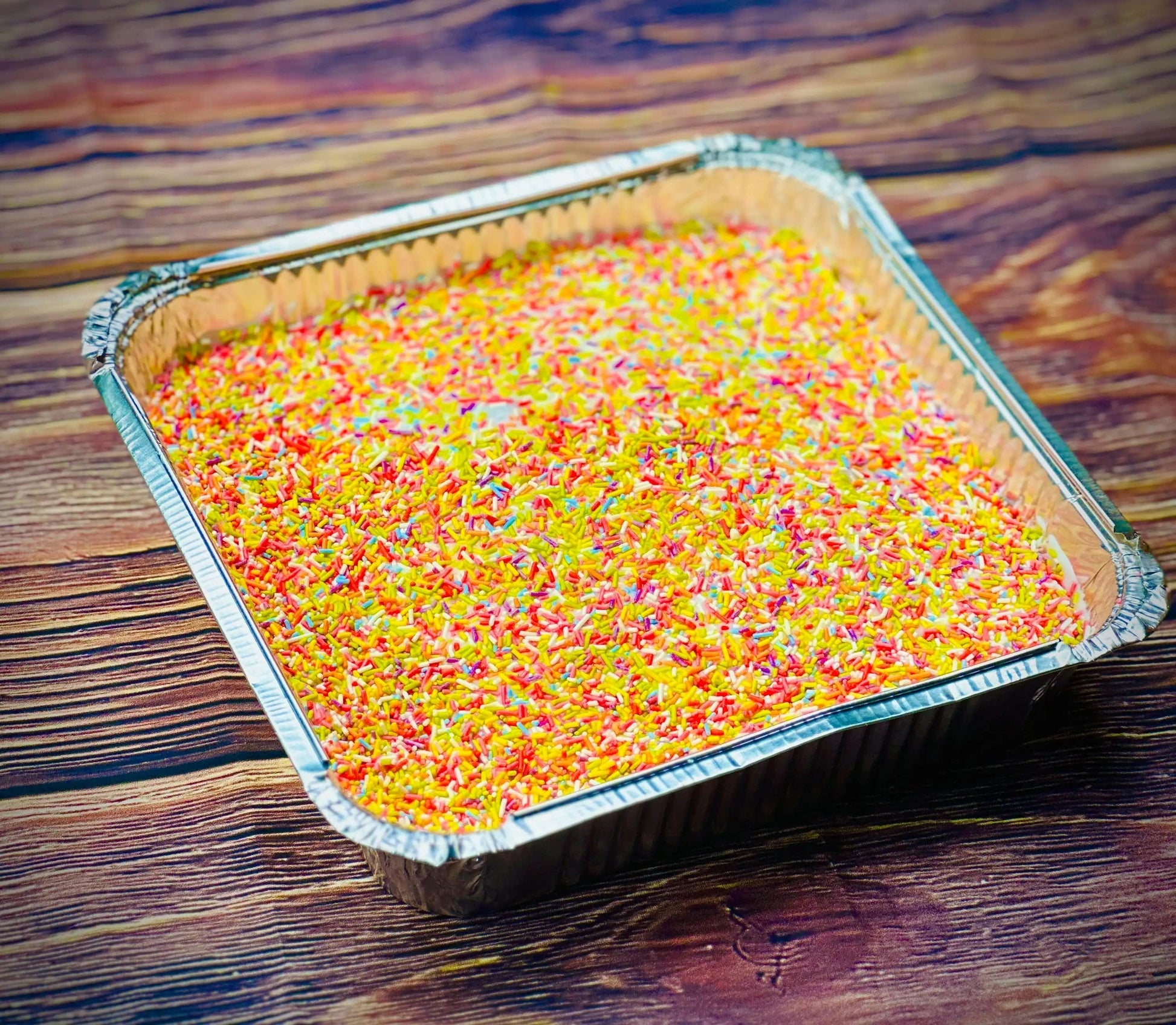 School cake tray with pink icing and rainbow sprinkles on a wooden table, freshly baked for same day delivery in Romford and Ilford, East London.