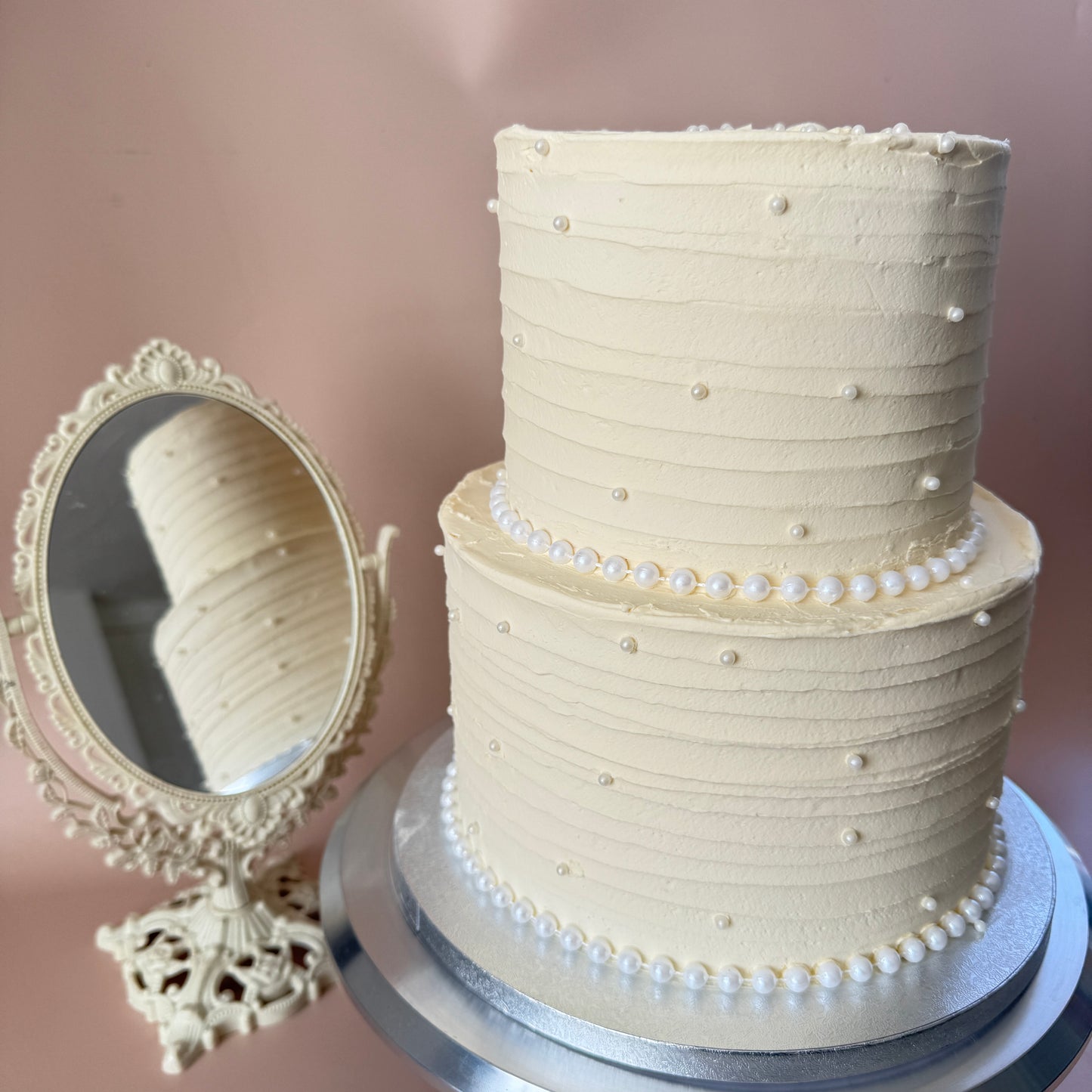 Two-tier ivory wedding cake with textured buttercream and edible pearl trim — custom cakes East London, Romford and Ilford.