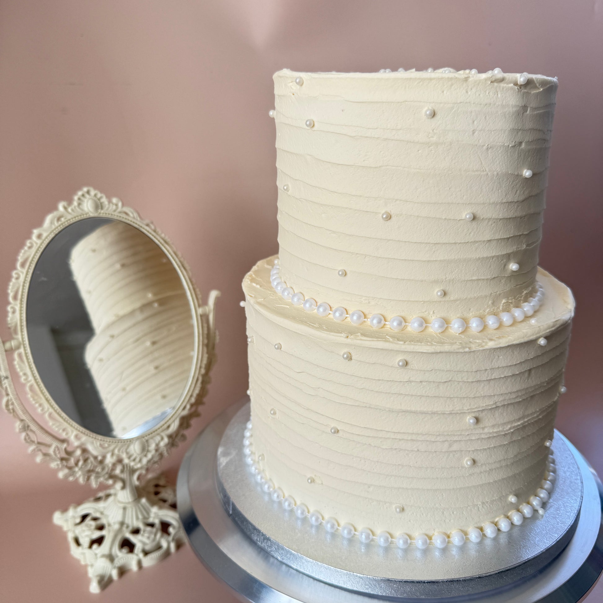 Two-tier ivory wedding cake with textured buttercream and edible pearl trim — custom cakes East London, Romford and Ilford.