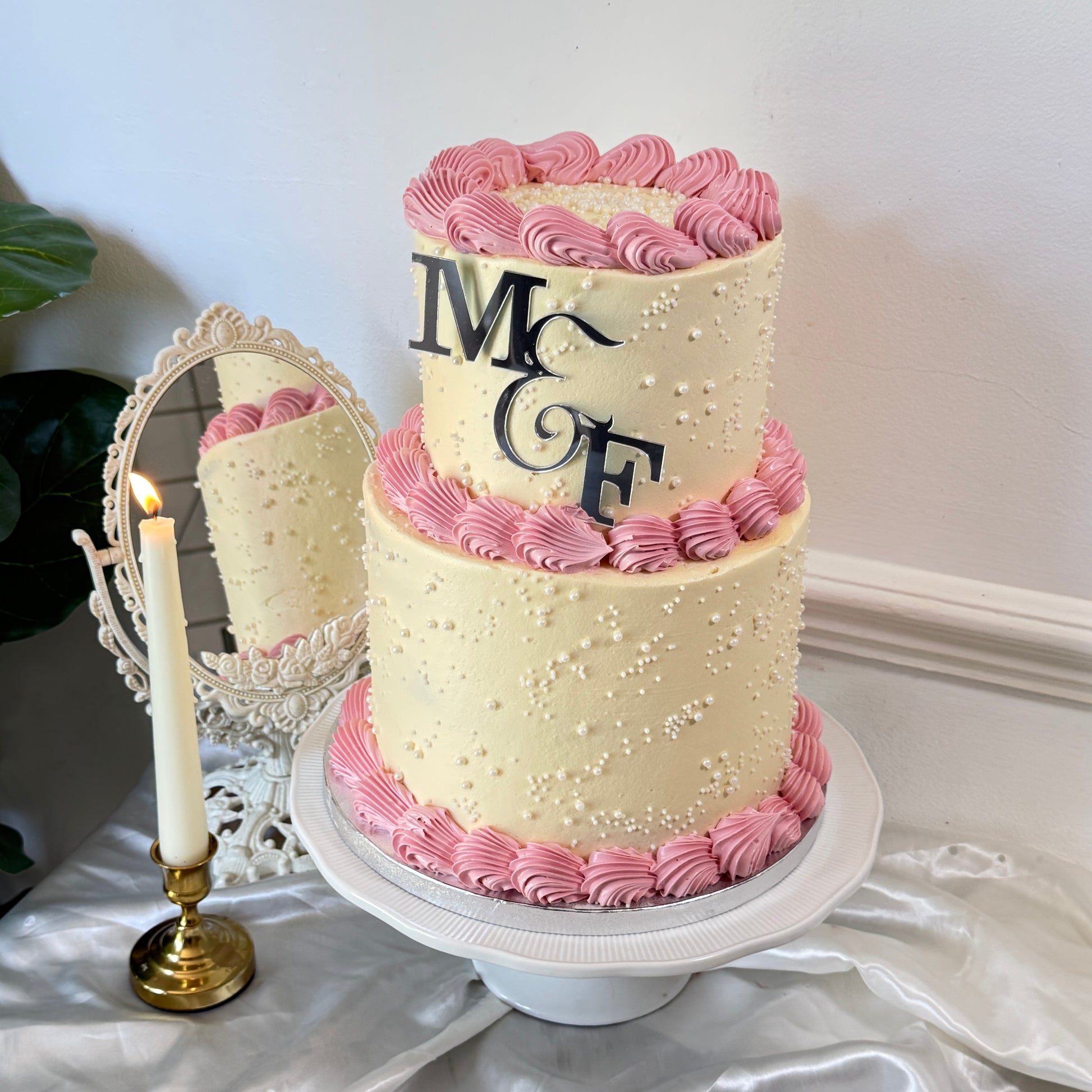 Two-tier ivory and pink pearl engagement cake with candle and mirror styling — custom celebration cakes East London, Romford and Ilford