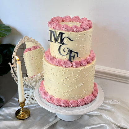 Two-tier ivory and pink pearl engagement cake with candle and mirror styling — custom celebration cakes East London, Romford and Ilford
